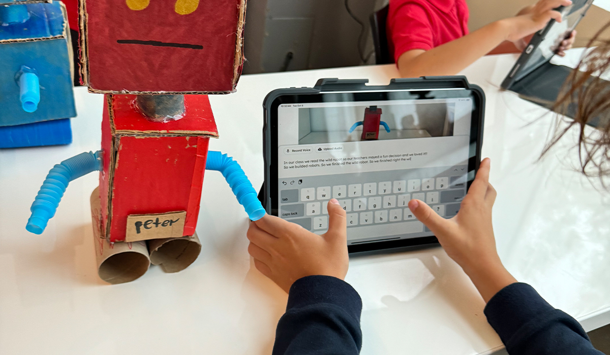 Students with a cardboard robot project and iPad